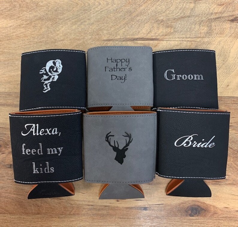 May include: Six different personalized can coolers. The coolers are made of black and gray faux leather. The text on the coolers includes "Happy Father's Day!", "Groom", "Bride", "Alexa, feed my kids", and a deer silhouette.