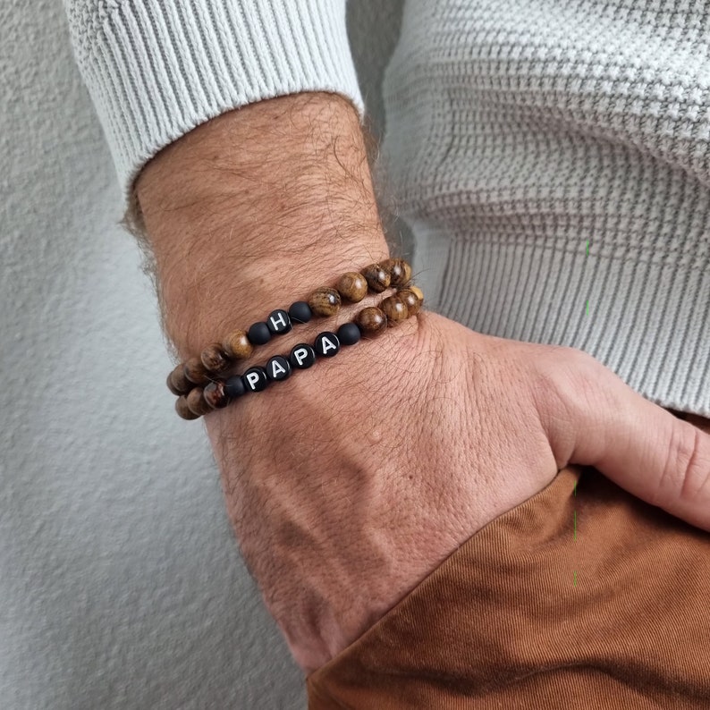 May include: Two beaded bracelets with black beads and white letter beads spelling "PAPA" and "H".