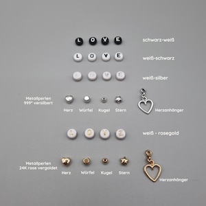 May include: A set of white, black and gold beads with the letters L, O, V and E. The beads are arranged in rows with different colour combinations. The beads are accompanied by small charms, including a heart, a cube, a sphere and a star. The text "Metallperlen 999&deg; versilbert" and "Metallperlen 24K rose vergoldet" is visible in the image. The text "schwarz-wei&szlig;", "wei&szlig;-schwarz", "wei&szlig;-silber", "wei&szlig; - rosegold" is also visible in the image.