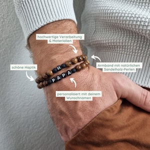 May include: A brown wooden bracelet with black beads that spell out "PAPA" and "H". The bracelet is on a person's wrist. The text "hochwertige Verarbeitung & Materialien", "sch&ouml;ne Haptik", "personalisiert mit deinem Wunschnamen", and "Armband mit nat&uuml;rlichen Sandelholz-Perlen" is written around the bracelet.