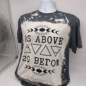 May include: A gray t-shirt with a bleached design featuring the text "As Above So Below" with a moon and sun symbol above and below the text. The design also includes three triangles and the number 20.