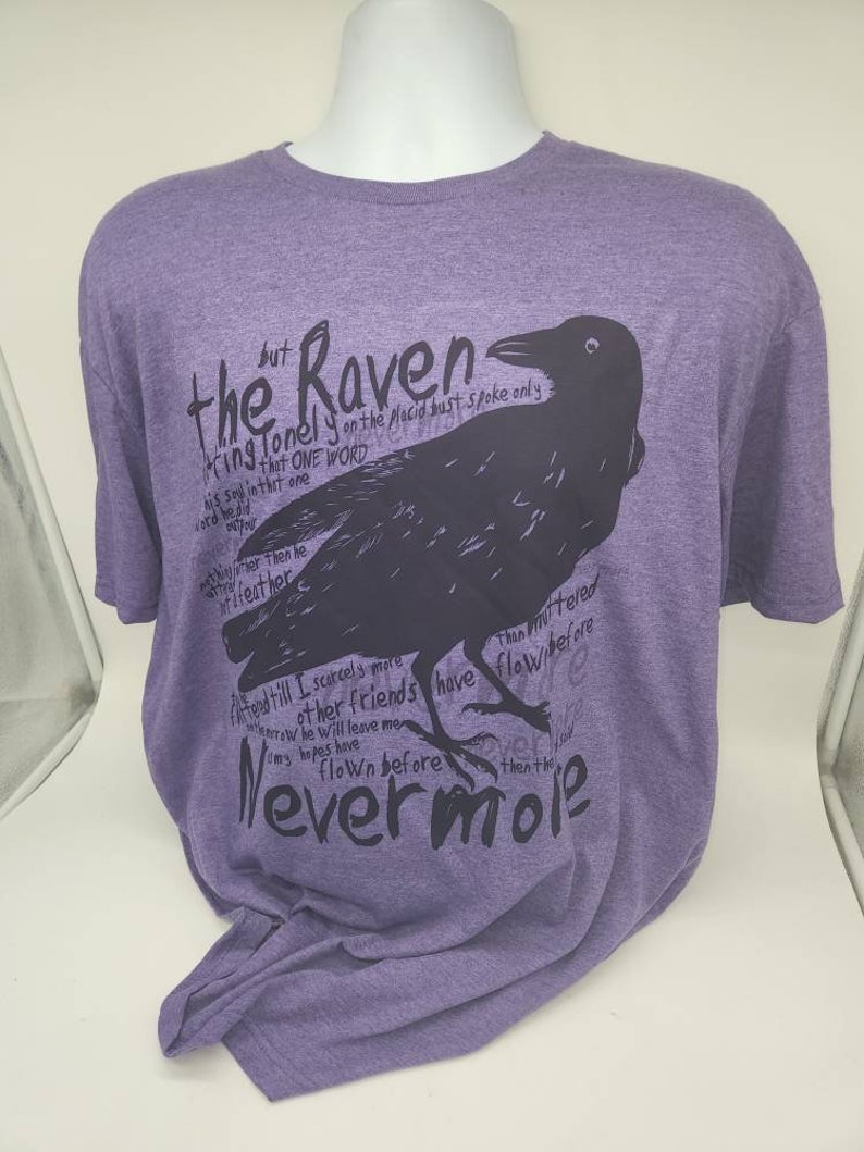 Op de afbeelding: Paars T-shirt met een zwarte raaf afbeelding en de tekst "the Raven" en "Nevermore".