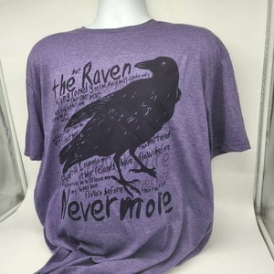 Op de afbeelding: Paars T-shirt met een zwarte raaf afbeelding en tekst die luidt "the Raven, King lonely on the Placid bust spoke only that one word... Nevermore".