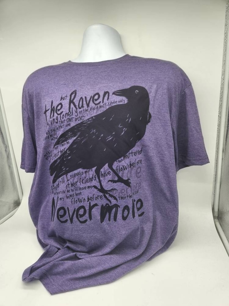 Op de afbeelding: Paars T-shirt met een zwarte raaf afbeelding en tekst die luidt "the Raven, King lonely on the Placid bust spoke only that one word... Nevermore".