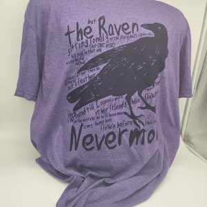 Op de afbeelding: Paars T-shirt met een zwart silhouet van een raaf en de tekst "the Raven sitting lonely on the placid bust spoke only this one word nevermore".