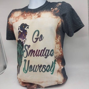 May include: A grey t-shirt with a bleached design featuring a sage bundle and the text "Go Smudge Yourself".