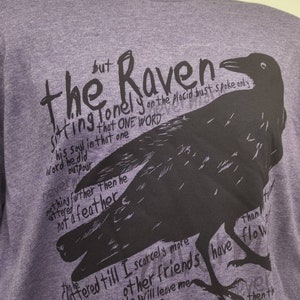 Op de afbeelding: Paars T-shirt met een zwarte raaf afbeelding en tekst die luidt "The Raven sitting lonely on the placid bust spoke only his soul in that one word he did outpour nothing further then he uttered not a feather fluttered till I scarcely more on the morrow other friends have flown before than my hopes have flown then the"