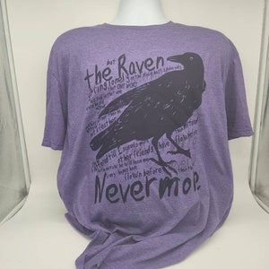 Op de afbeelding: Paars T-shirt met een zwarte raaf afbeelding en tekst die "The Raven" en "Nevermore" zegt.