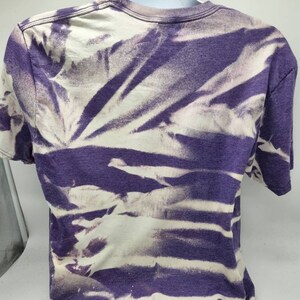 May include: Purple and white tie-dye t-shirt. The shirt has a faded look with white streaks on a purple background.