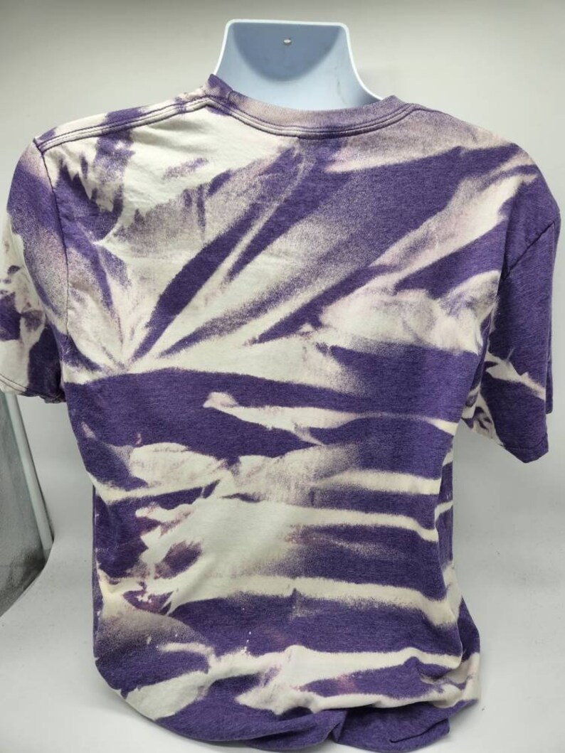 May include: Purple and white tie-dye t-shirt. The shirt has a faded look with white streaks on a purple background.