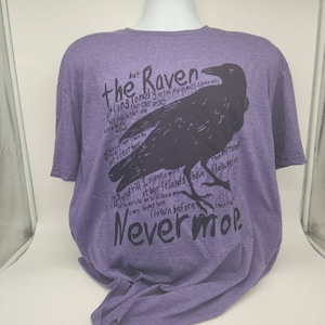 Op de afbeelding: Paars T-shirt met een zwarte raaf afbeelding en tekst die "The Raven" en "Nevermore" zegt.