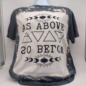 May include: A gray t-shirt with a bleached design featuring the text "As Above So Below" with a crescent moon and sun graphic.
