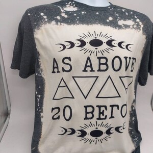 May include: A gray t-shirt with a bleached design featuring the text "As Above So Below" with a sun and moon symbol above and below the text. The design also includes three triangles.
