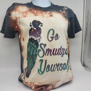 May include: A grey t-shirt with a bleached design featuring a sage smudge stick and the text "Go Smudge Yourself".