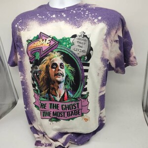 May include: Purple tie-dye t-shirt with a bleached effect. The shirt features a graphic of a character from the movie Beetlejuice, with the text "Be the Ghost with the Most, Babe" and "Never Trust the Living".