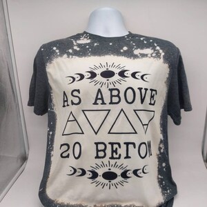 May include: A gray t-shirt with a bleached design featuring the text "As Above So Below" with a crescent moon and sun symbol above and below the text.