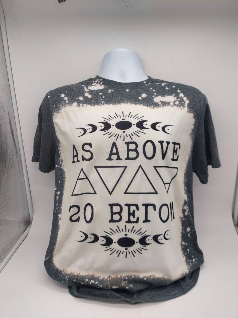 May include: A gray t-shirt with a bleached design featuring the text "As Above So Below" with a crescent moon and sun symbol above and below the text.