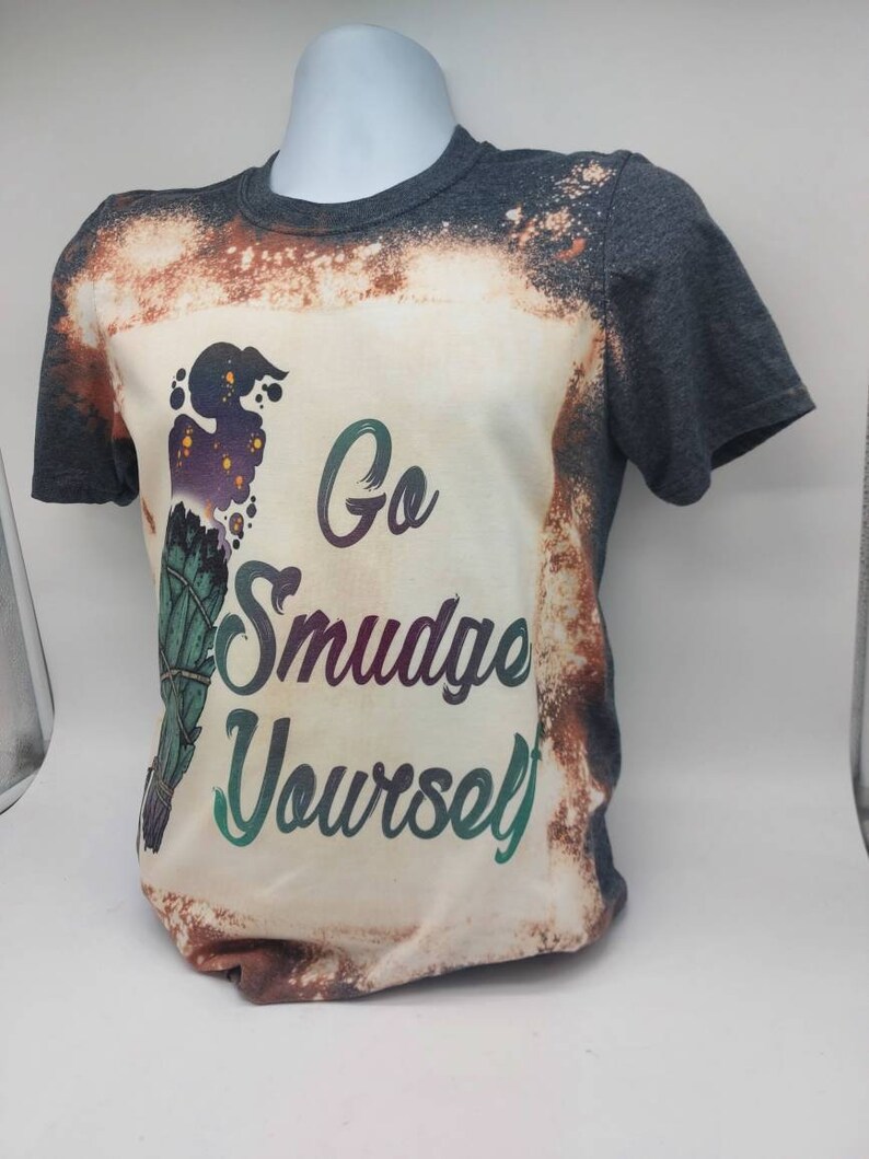 May include: A grey t-shirt with a bleached effect and a graphic of a smudge stick with the text "Go Smudge Yourself".