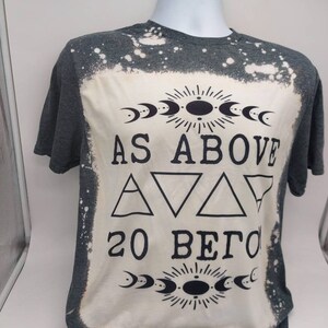 May include: A gray t-shirt with a bleached design featuring the text "As Above So Below" with a moon and sun symbol above and below the text. The shirt has a distressed look with white splatter paint.