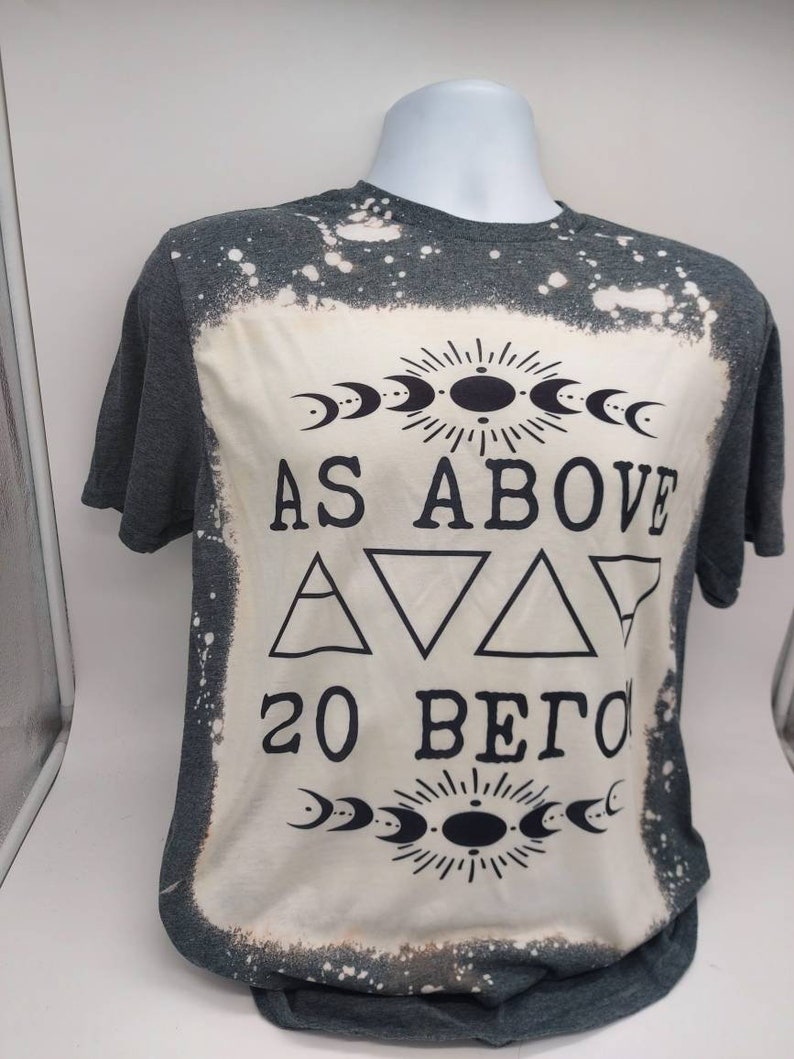 May include: A gray t-shirt with a bleached design featuring the text "As Above So Below" with a moon and sun symbol above and below the text. The shirt has a distressed look with white splatter paint.