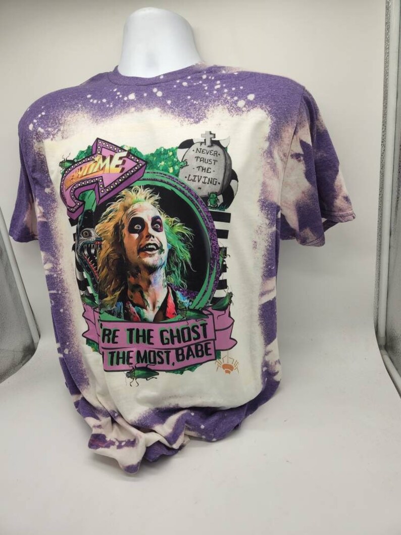 May include: Purple and white bleached t-shirt with a graphic print of a character from the movie Beetlejuice. The graphic includes the text "Be the ghost the most, babe" and "Never trust the living".