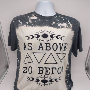May include: A gray t-shirt with a bleach-splattered design. The shirt features a black graphic with the text "As Above So Below" and a symbol with three triangles.