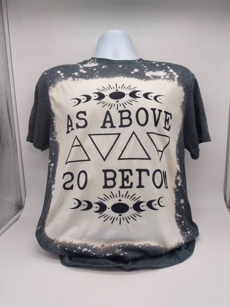 May include: A gray t-shirt with a bleached design featuring the text "As Above So Below" with a crescent moon and sun graphic.