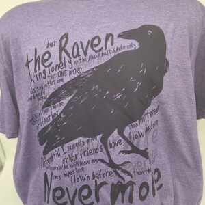 Op de afbeelding: Paarse T-shirt met een zwarte raaf afbeelding en tekst die luidt "Maar de Raaf, eenzaam op de rustige buste, sprak slechts &eacute;&eacute;n woord..."