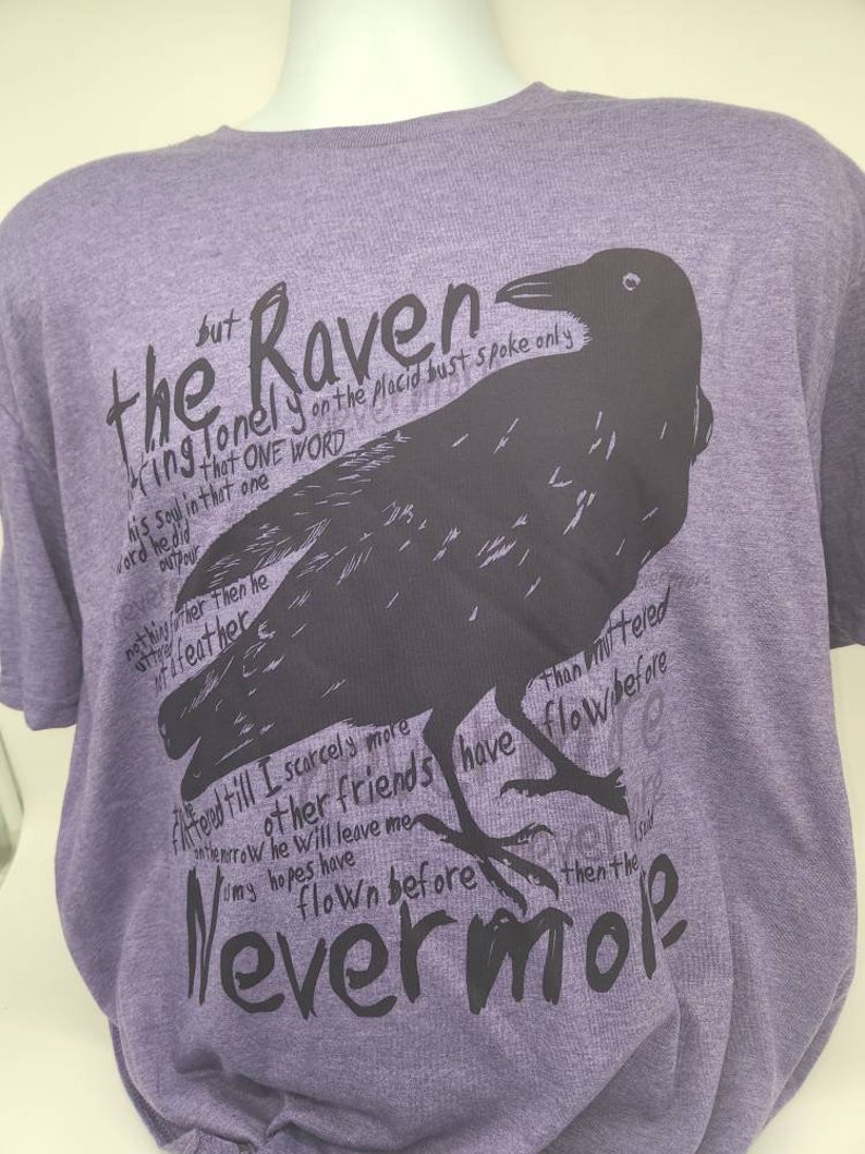 Op de afbeelding: Paarse T-shirt met een zwarte raaf afbeelding en tekst die luidt "Maar de Raaf, eenzaam op de rustige buste, sprak slechts &eacute;&eacute;n woord..."