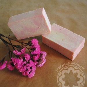 Op de afbeelding: Twee handgemaakte zeepjes met een roze en witte swirl-design. De zeep ligt op een bruine papieren achtergrond met roze bloemen.
