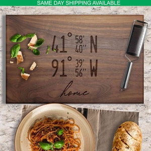 May include: A wooden chopping board with the coordinates 41° 58' 40" N 91° 39' 56" W and the word "home" engraved on it. The board is brown and has a natural wood grain. There is a small metal grater on the board.