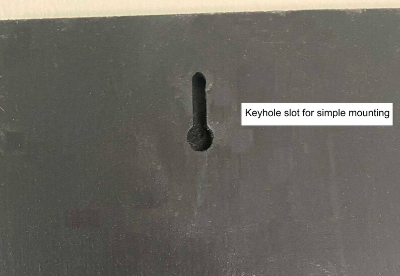May include: A close-up of a black surface with a keyhole slot for simple mounting. The keyhole slot is a common feature for hanging items on a wall.
