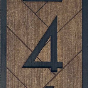 May include: Black house numbers 246 on a wooden background with a chevron pattern. The numbers are painted black and are centered on the wood.