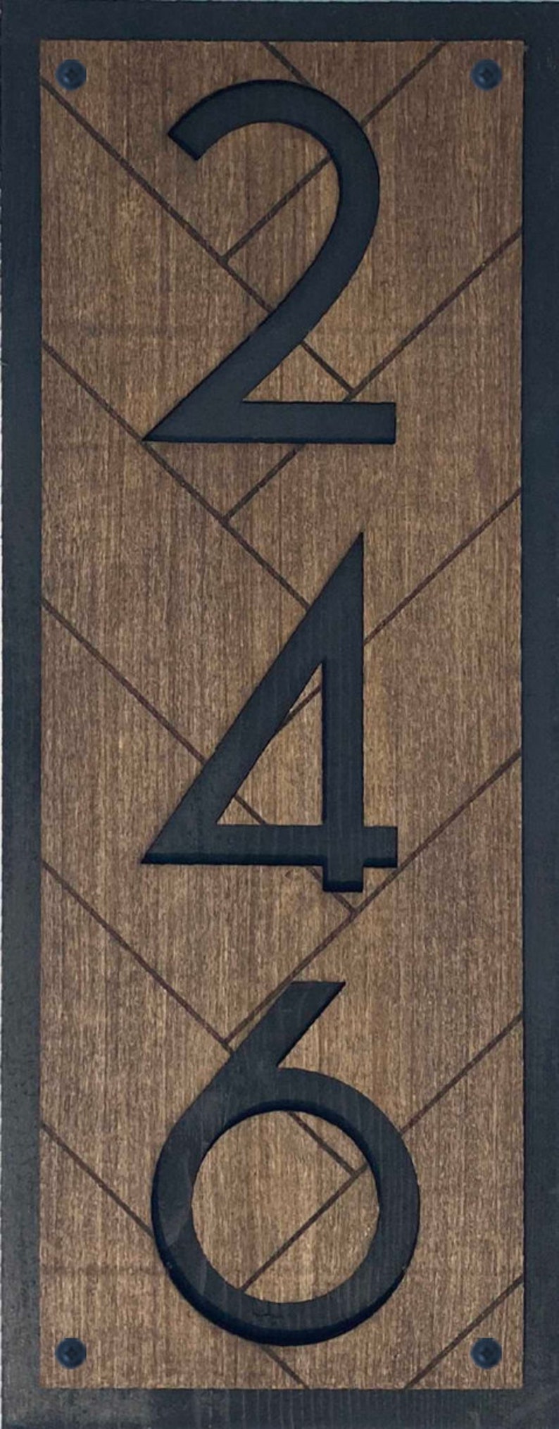 May include: Black house numbers 246 on a wooden background with a chevron pattern. The numbers are painted black and are centered on the wood.