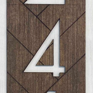 May include: White numbers 246 on a brown wooden background with a chevron pattern. The numbers are cut out of the wood and have a white painted finish.