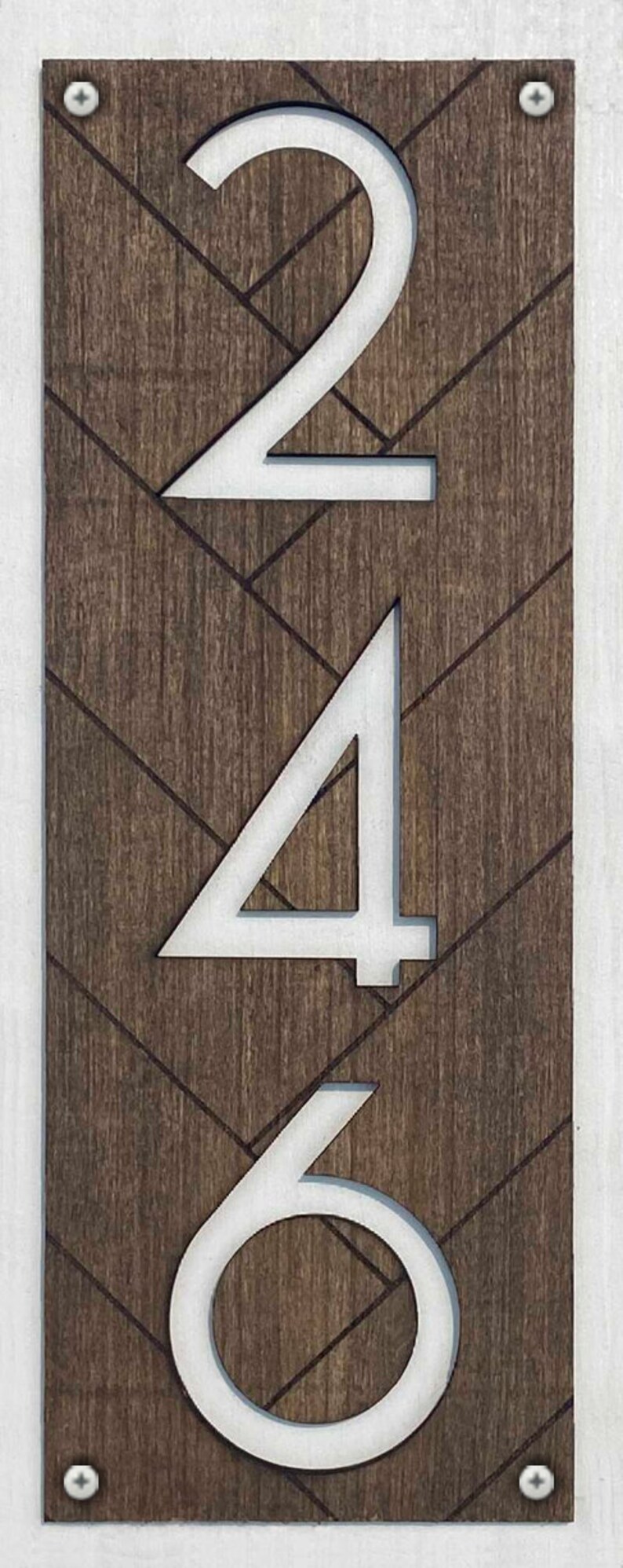 May include: White numbers 246 on a brown wooden background with a chevron pattern. The numbers are cut out of the wood and have a white painted finish.