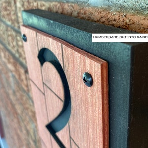 May include: A close-up of a wooden house number plaque with the number "2" cut out of the raised panel. The plaque is painted black and has a wood grain finish. The number is cut out of the raised panel and is black.