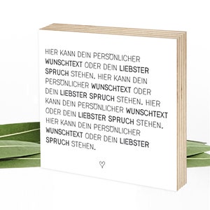Könnte beinhalten: Ein quadratischer Holzblock mit weißer Vorderseite und schwarzem deutschen Textaufdruck: HIER KANN DEIN PERSÖNLICHER WUNSCHTEXT ODER DEIN LIEBSTER SPRUCH STEHEN. Ein kleines schwarzes Herz-Symbol ist mittig am unteren Rand aufgedruckt.