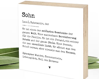 May include: A square wooden block with a white front face featuring black printed German text defining the word Sohn. The text includes phonetic pronunciation, grammatical classification, a descriptive paragraph, synonyms, and a small heart icon.