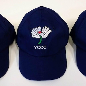 May include: Three navy blue baseball caps with a white and red floral design embroidered on the front. Each cap has the white text "YCCC" below the floral design. The caps have a curved peak and a button on top.