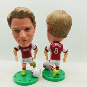 May include: A bobblehead figurine of a soccer player wearing a red and white soccer uniform with the number 8 on the back. The player is holding a soccer ball and is standing on a green base.
