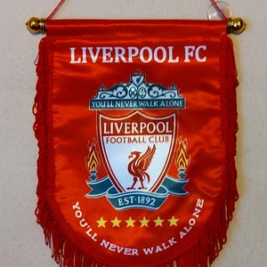 May include: Red and white Liverpool FC pennant with a red fringe. The pennant features the team's crest, which includes a red bird, and the text "You'll Never Walk Alone".