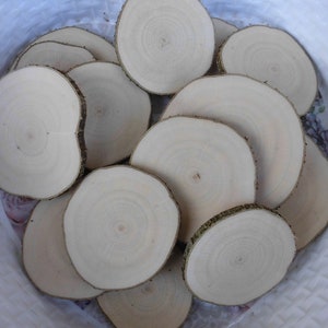 Könnte beinhalten: Ein Stapel runder Holzscheiben, jede mit einem natürlichen Holzmaserungsmuster. Die Scheiben sind in verschiedenen Größen und in einer weißen Schüssel angeordnet.