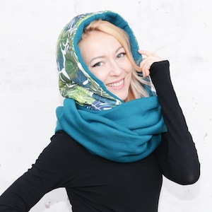 Könnte beinhalten: Ein türkisfarbener Kapuzen-Schal mit einem grünen und weißen Blumendruck. Der Schal ist aus weichem, kuscheligem Stoff gefertigt und perfekt, um sich im Winter warm zu halten.