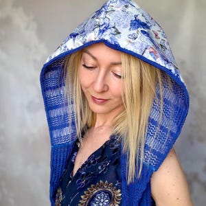 May include: A blue hooded scarf with a floral pattern and a blue knit trim. The hood features a white background with blue flowers and birds. The scarf is a vibrant blue color.