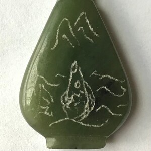 May include: A green jade pendant in the shape of a bottle with a gold top. The bottle has a white design of mountains and waves.