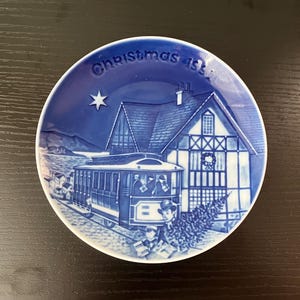 May include: Blue and white Christmas plate with a scene of a house, a streetcar, and people carrying a Christmas tree. The plate reads "Christmas 1969".