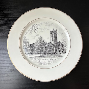 May include: A round white ceramic plate with a thin gold rim. The center features a detailed black ink sketch of the Foundry Methodist Church in Washington, D.C., with the text Foundry Methodist Church, Washington, D.C., 1814 printed below.