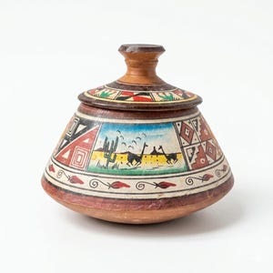 May include: A hand-painted ceramic jar with a lid. The jar features a brown base and lid, with colorful geometric and landscape designs. The landscape depicts cacti, mountains, and running animals. The jar is approximately 5 inches tall.