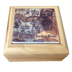 May include: A small, square wooden box with a decorative tile top. The tile features a vintage map design with the words "Jordan River" and other text. The box is made of light-colored wood.